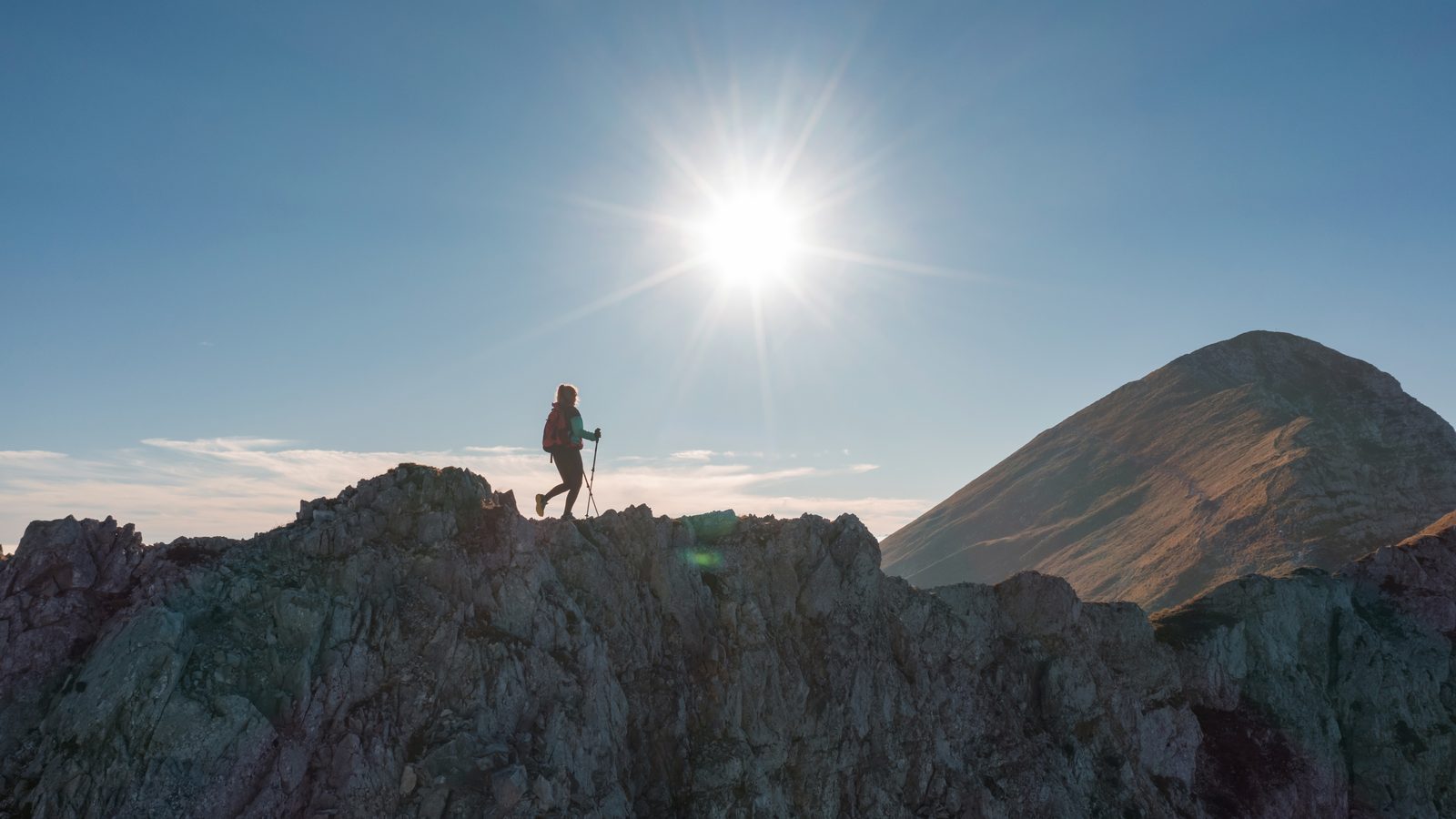 A lone walker silhouetted on a rocky ridge against the sun