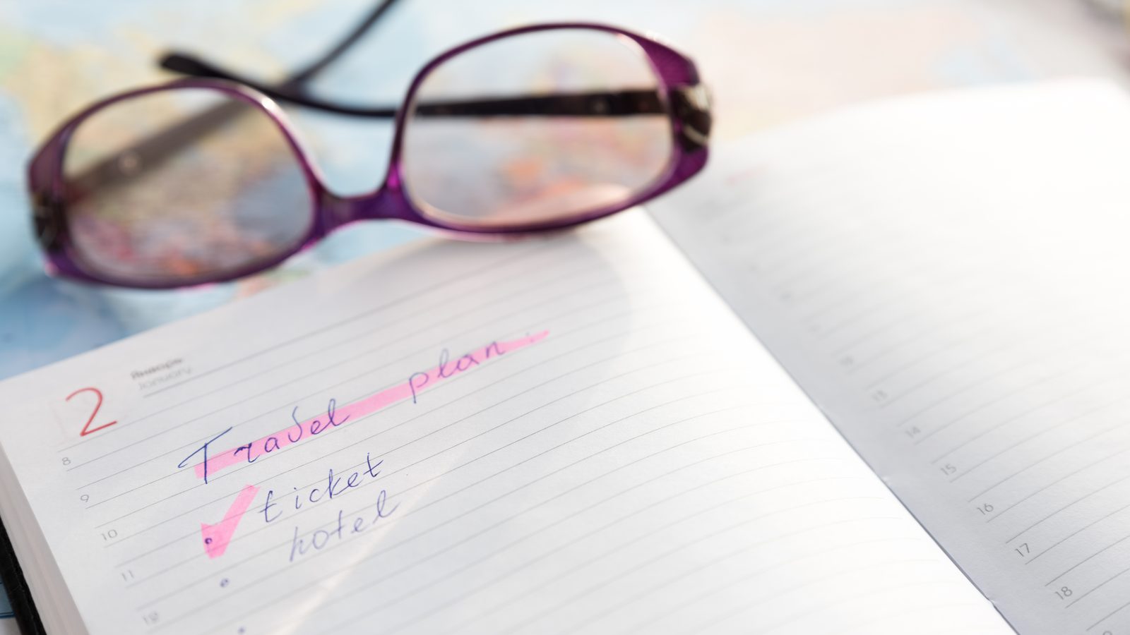 A travel plan written out by hand in a notebook, reading glasses beside it