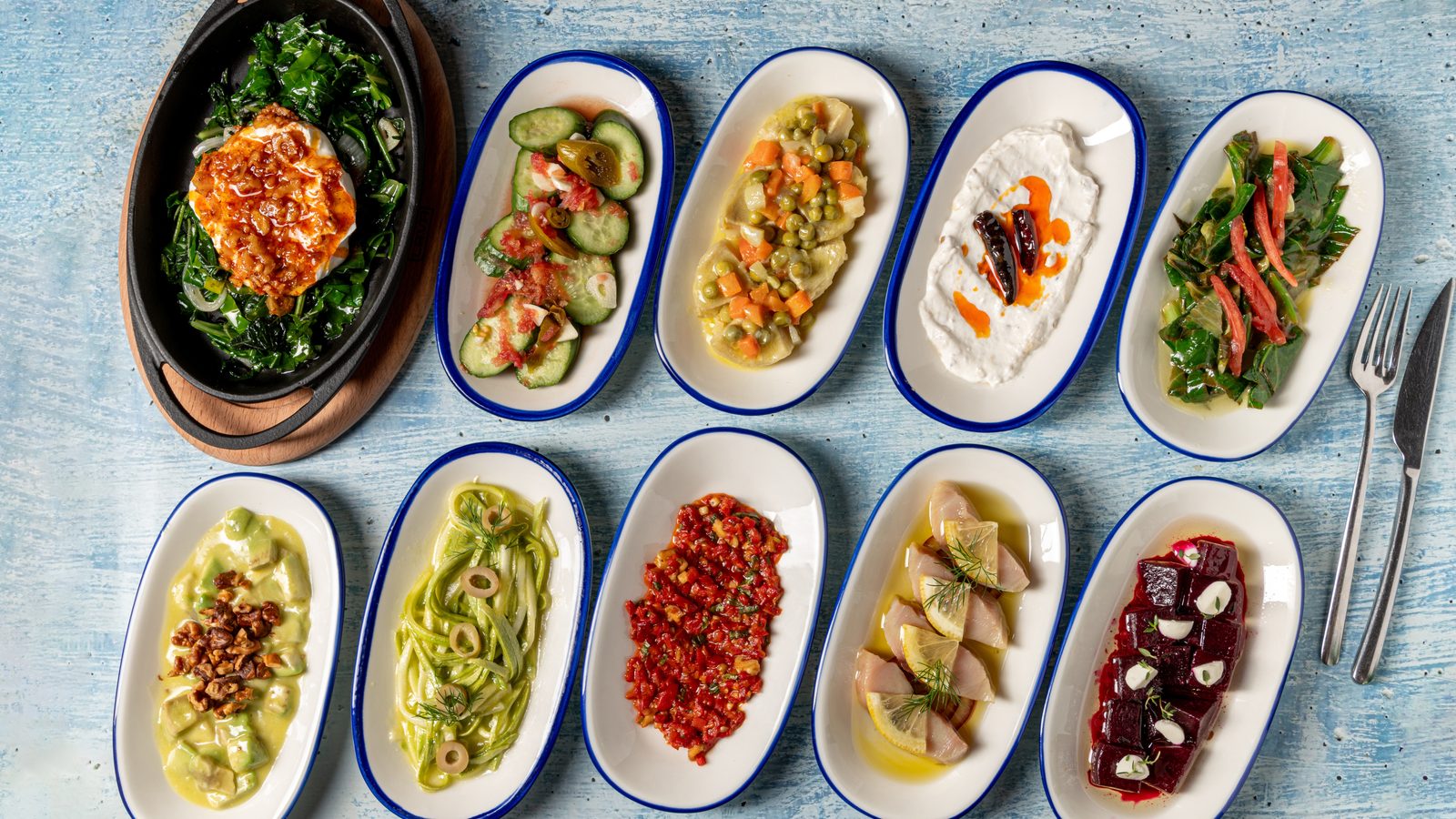 Plates of Turkish meze — yoghurt, herbs, aubergine, beetroot and pepper dishes — laid out on a blue table